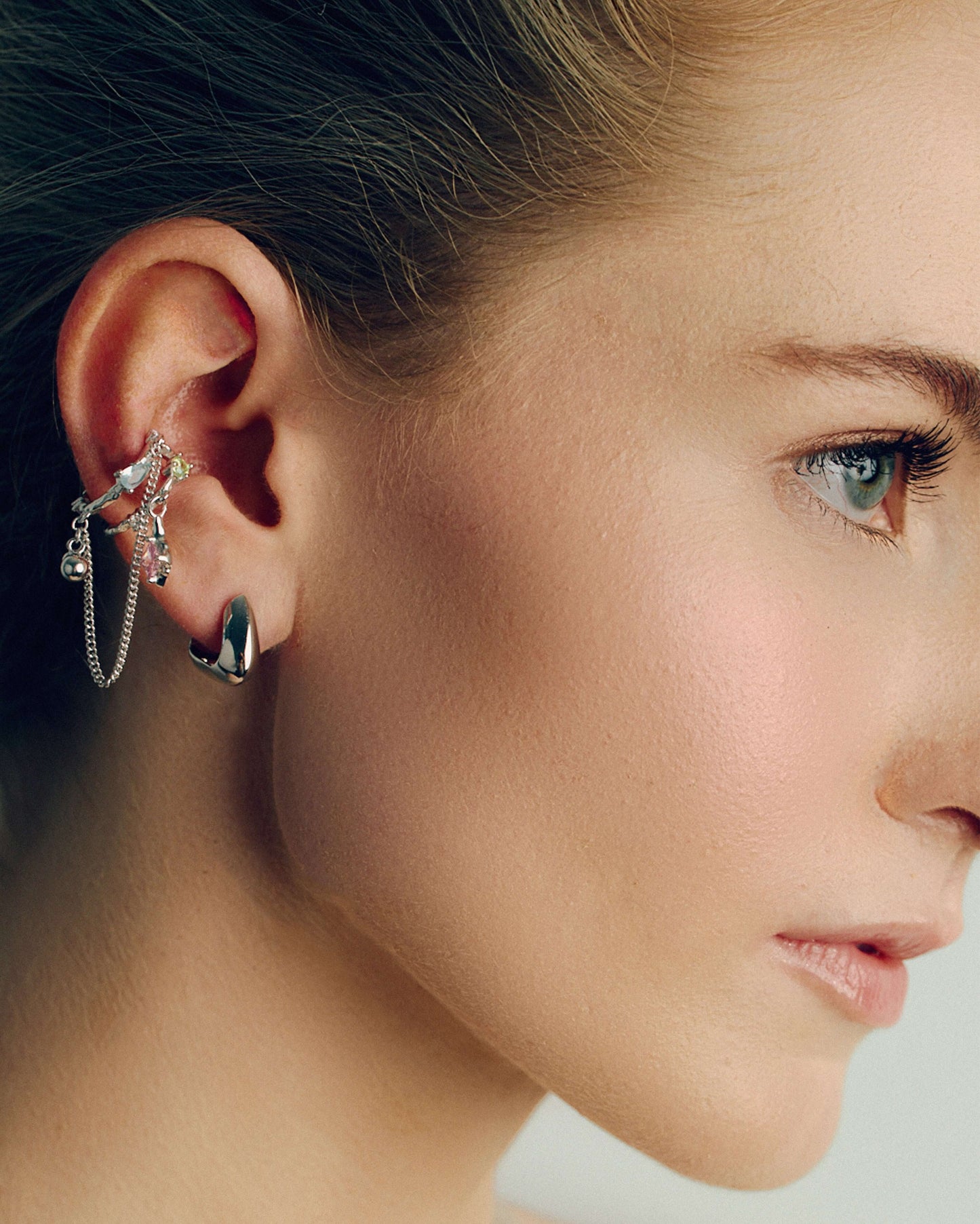 Gold and silver ear cuffs with dangling chains, charms, and colorful cubic zirconia stones. Non-pierced adjustable cartilage cuffs featuring teardrop and square-cut gems for a bold, playful, and trendy statement look.