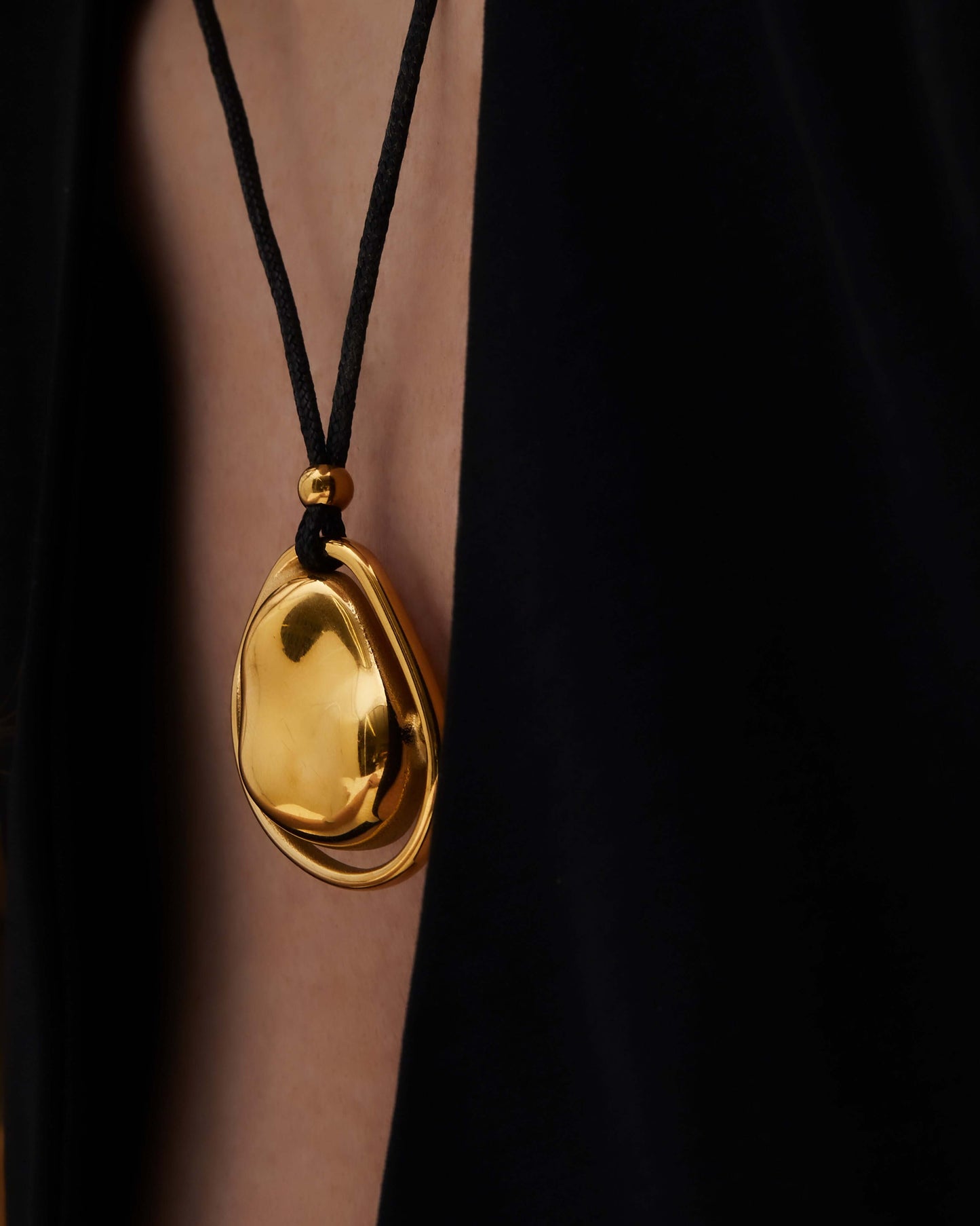 Oversized bean pendant on a polished black tie chain with 18k gold or silver finish, adjustable length, sleek modern minimalist design.
