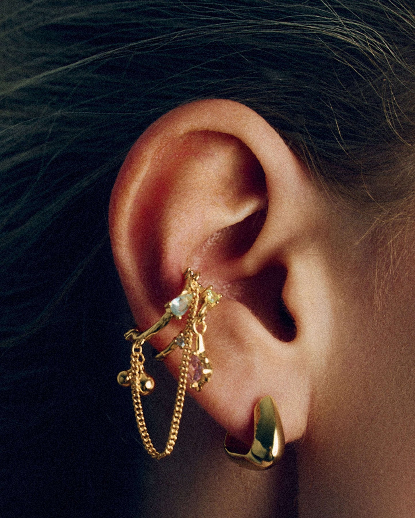 Gold and silver ear cuffs with dangling chains, charms, and colorful cubic zirconia stones. Non-pierced adjustable cartilage cuffs featuring teardrop and square-cut gems for a bold, playful, and trendy statement look.