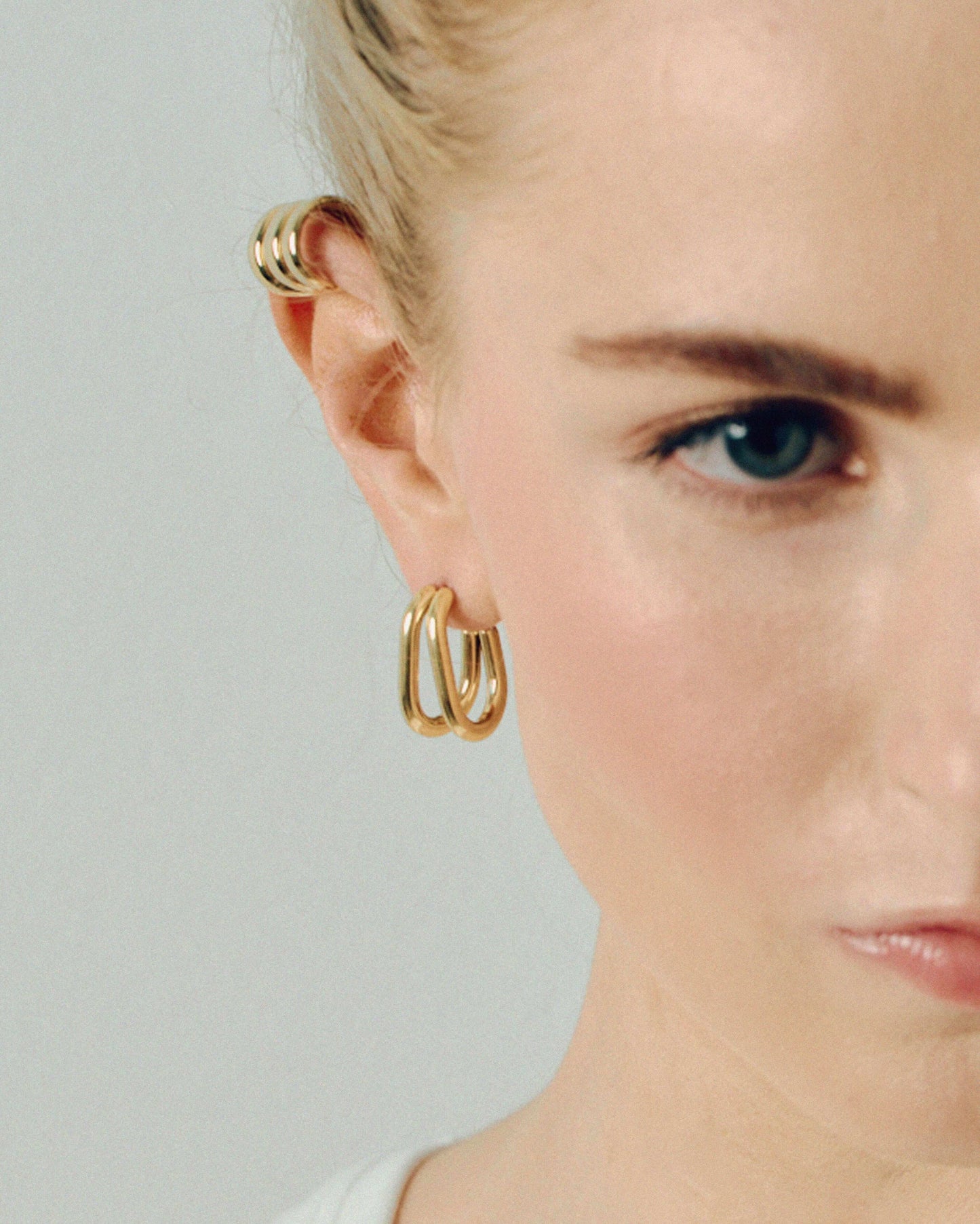 Gold double hoop earrings featuring two thick, sculptural curved bands with a polished high-shine finish. Modern layered design with secure post backs, creating a bold yet minimalist statement. Perfect for everyday wear or adding a stylish, contemporary touch to any outfit.