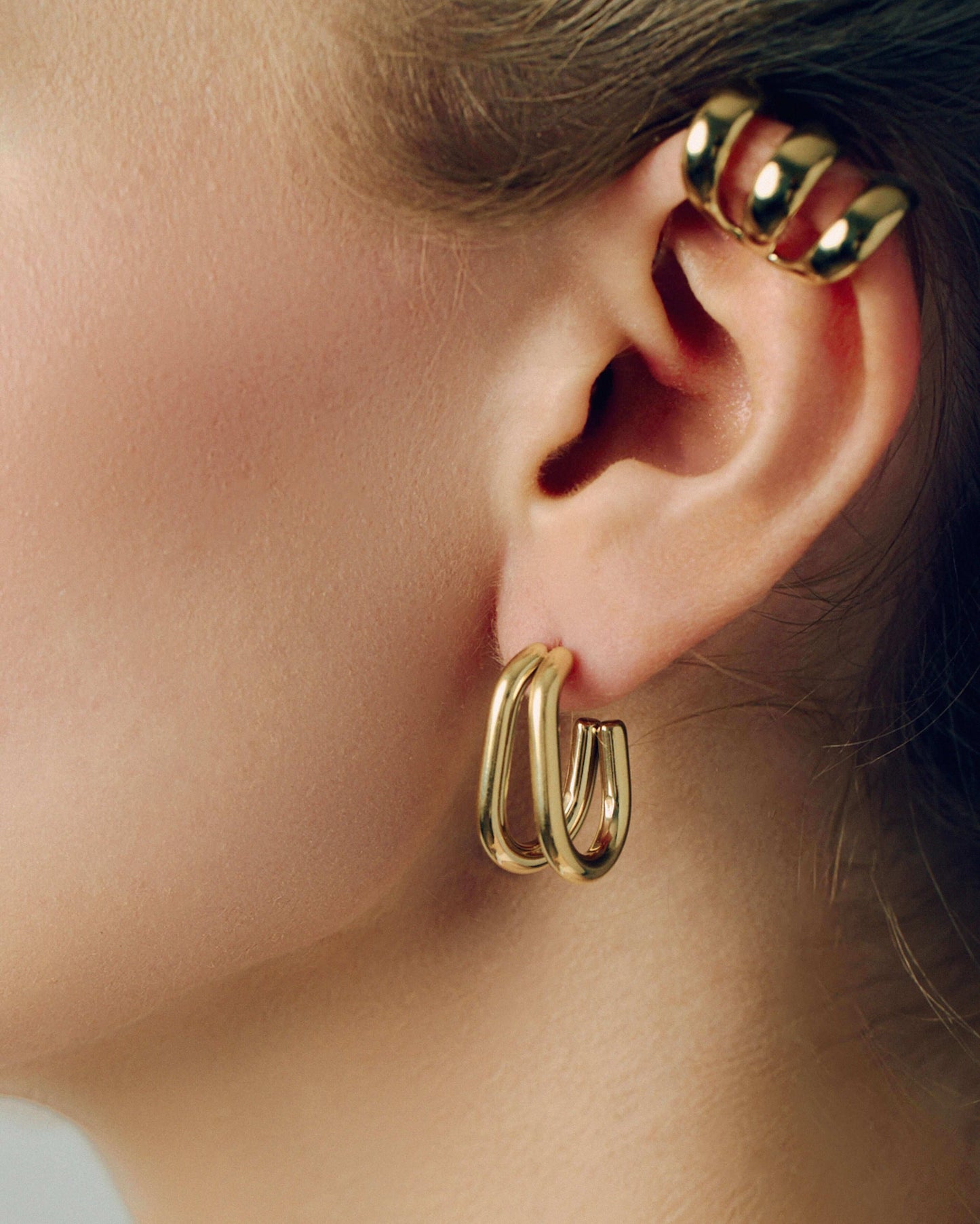 Gold double hoop earrings featuring two thick, sculptural curved bands with a polished high-shine finish. Modern layered design with secure post backs, creating a bold yet minimalist statement. Perfect for everyday wear or adding a stylish, contemporary touch to any outfit.