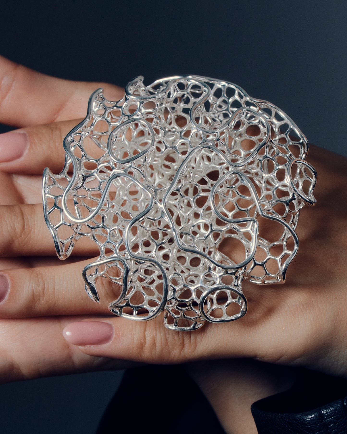 Close-up of a sculptural open-work statement ring featuring organic, lattice-like curves that flow across the fingers. The bold, artistic design catches light and shadow, creating a striking balance of size and airiness. Perfect for modern, contemporary, and architectural jewelry lovers who appreciate wearable art.