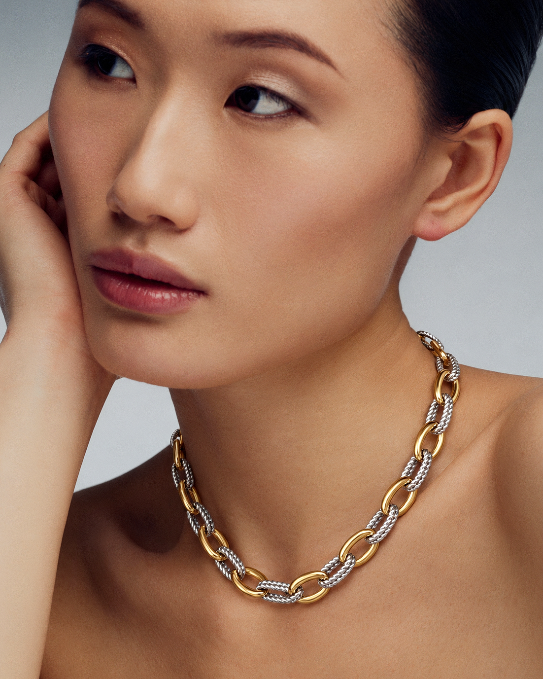 A close-up of a woman wearing a chunky gold chain necklace with alternating gold and silver pavé-set links