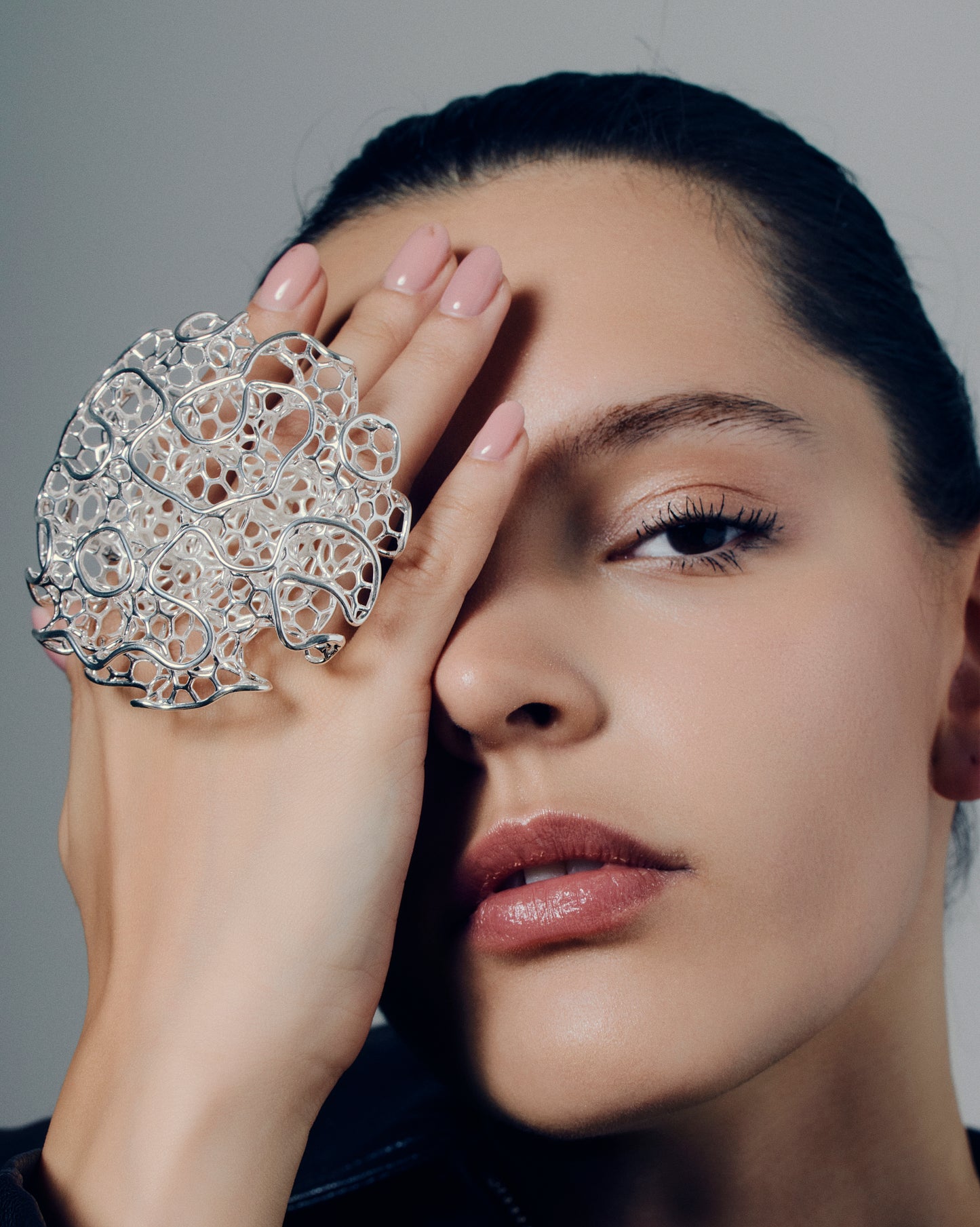 Close-up of a sculptural open-work statement ring featuring organic, lattice-like curves that flow across the fingers. The bold, artistic design catches light and shadow, creating a striking balance of size and airiness. Perfect for modern, contemporary, and architectural jewelry lovers who appreciate wearable art.
