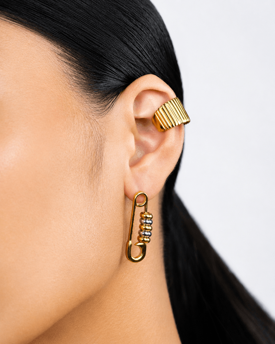 Gold safety pin earrings with silver bead details worn on ear, chunky statement earrings for women, modern two tone jewelry, edgy minimalist gold hoop earrings, trendy everyday fashion accessory, unique punk inspired earrings, stainless steel safety pin d