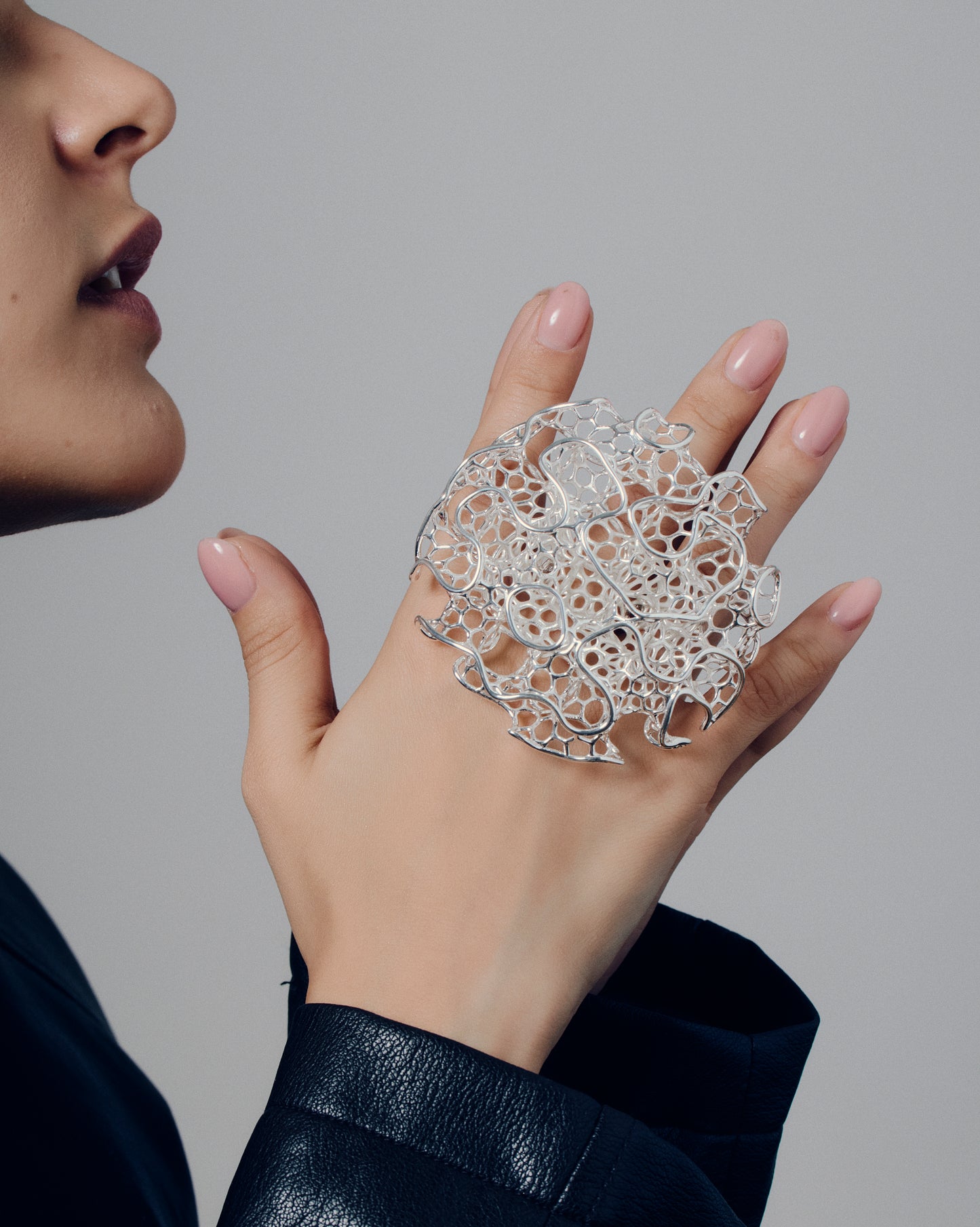Close-up of a sculptural open-work statement ring featuring organic, lattice-like curves that flow across the fingers. The bold, artistic design catches light and shadow, creating a striking balance of size and airiness. Perfect for modern, contemporary, and architectural jewelry lovers who appreciate wearable art.