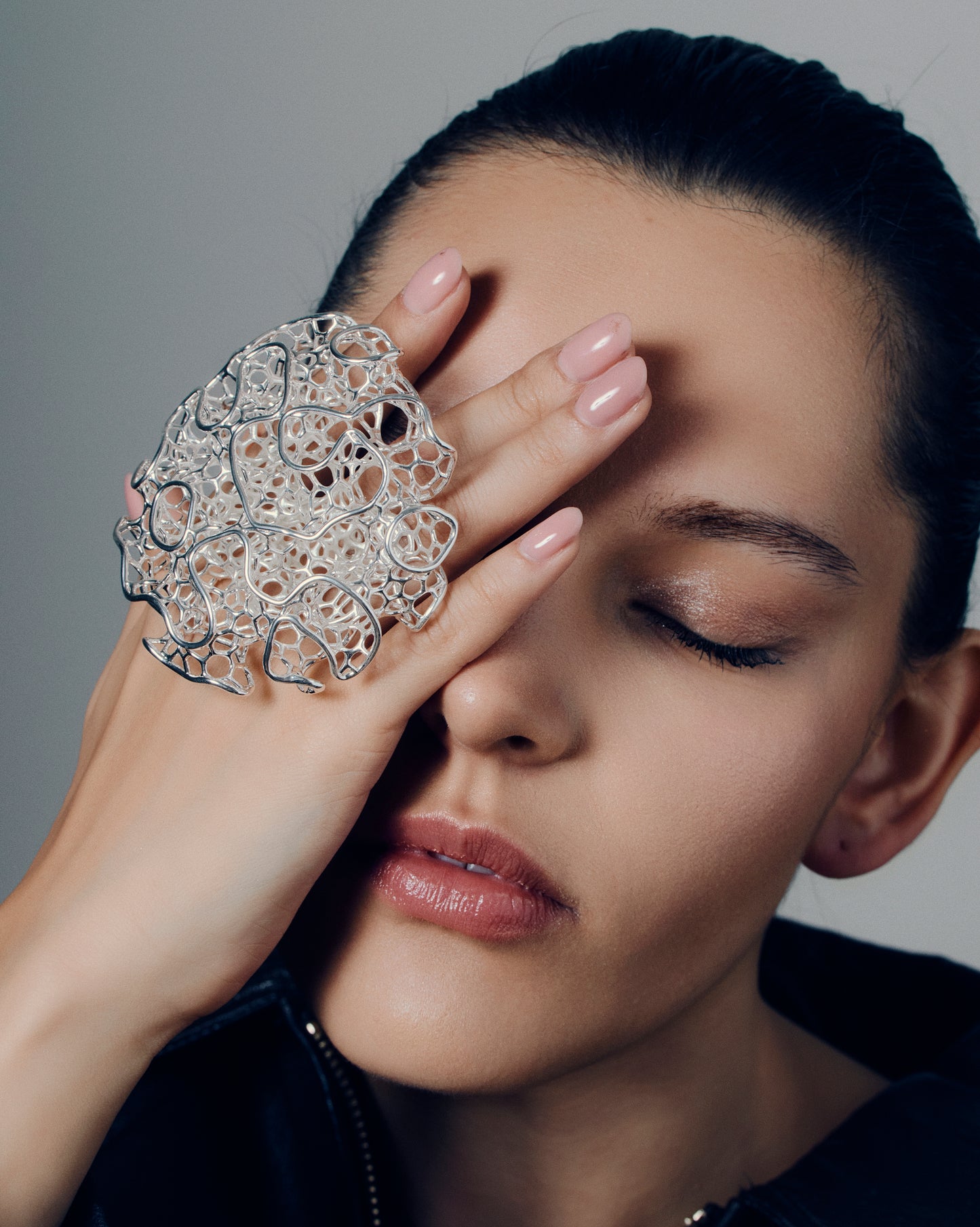 Close-up of a sculptural open-work statement ring featuring organic, lattice-like curves that flow across the fingers. The bold, artistic design catches light and shadow, creating a striking balance of size and airiness. Perfect for modern, contemporary, and architectural jewelry lovers who appreciate wearable art.