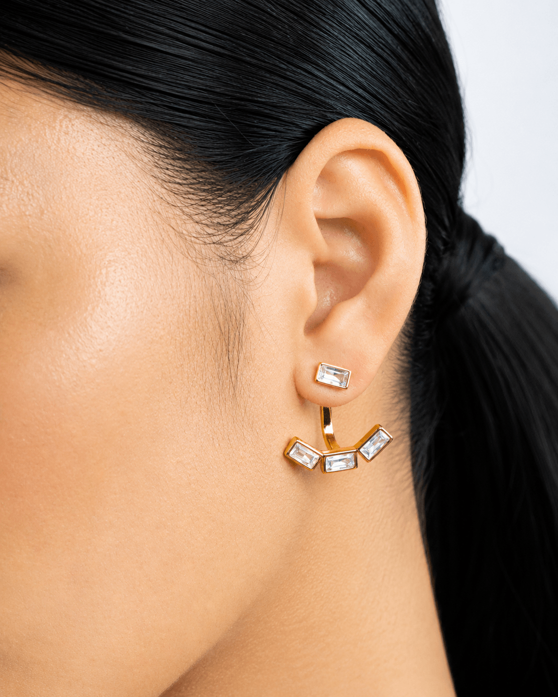 Detachable baguette zircon ear jacket earrings in gold finish displayed on a soft neutral background. Modern geometric stud earrings with removable ear jacket design, featuring sparkling rectangular CZ stones and minimalist contemporary styling for everyday wear and statement looks.