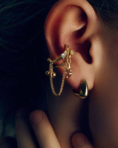 Gold and silver ear cuffs with dangling chains, charms, and colorful cubic zirconia stones. Non-pierced adjustable cartilage cuffs featuring teardrop and square-cut gems for a bold, playful, and trendy statement look.