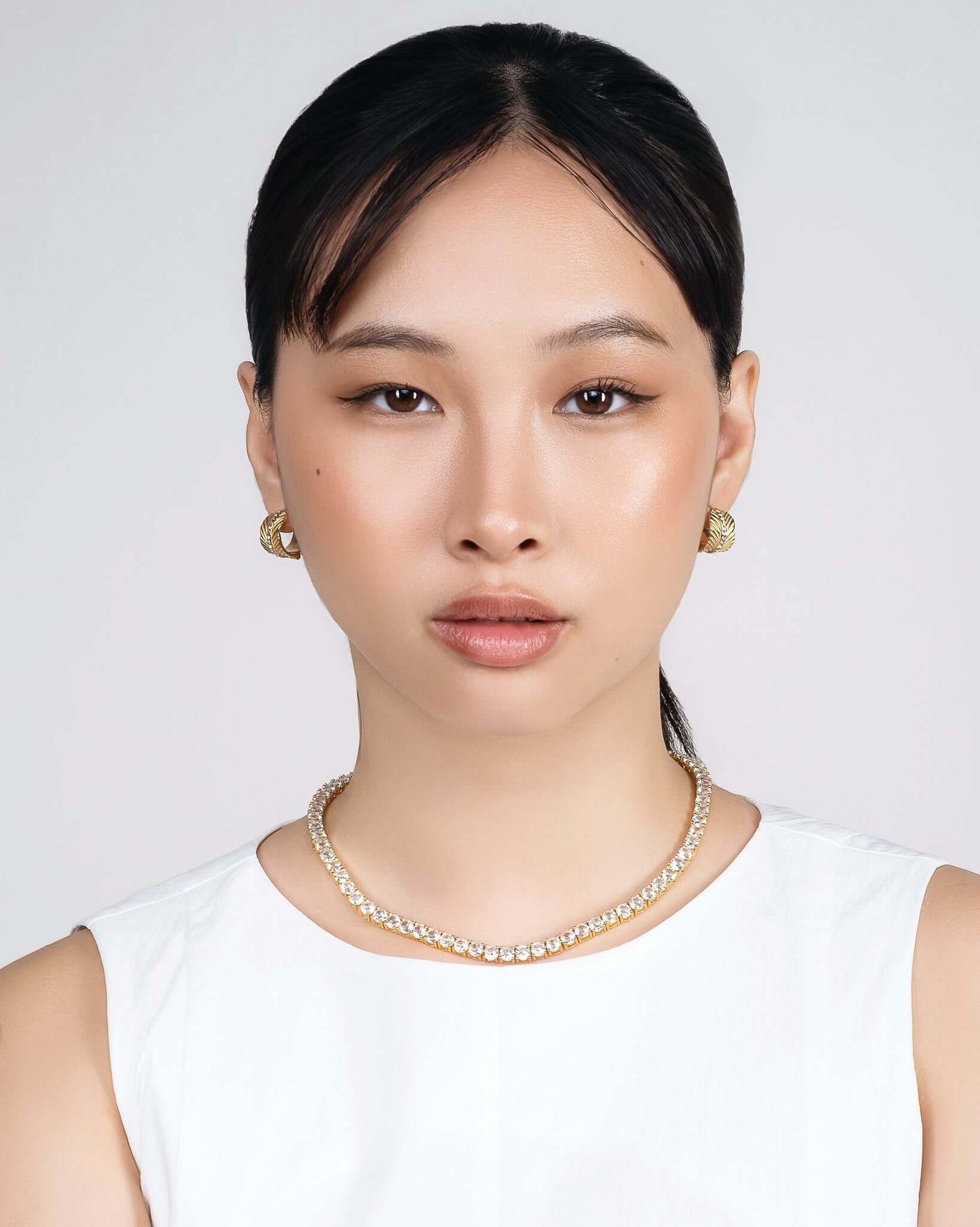 Woman wearing chunky gold CZ hoop earrings with textured sunburst pattern and crystal center stripe, statement gold huggie hoop earrings for women, trendy luxury gold earrings, modern fashion jewelry, bold everyday hoop earrings, stylish gold crystal earrings model closeup.