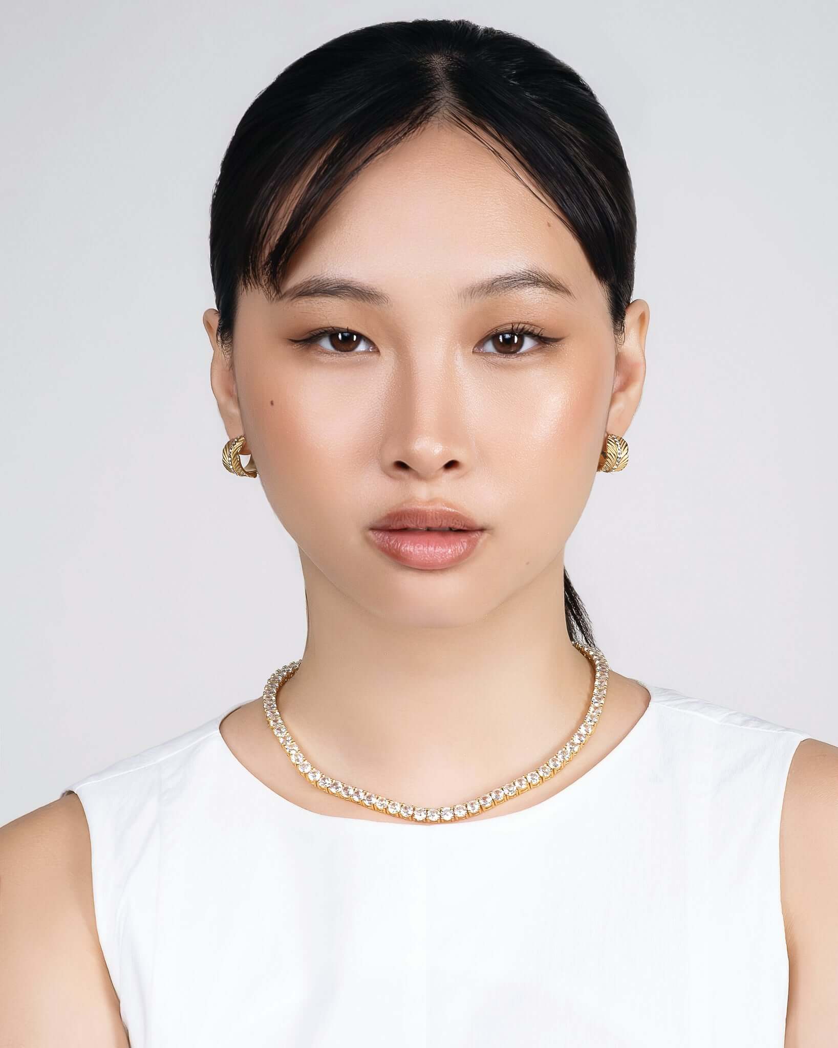 Woman wearing chunky gold CZ hoop earrings with textured sunburst pattern and crystal center stripe, statement gold huggie hoop earrings for women, trendy luxury gold earrings, modern fashion jewelry, bold everyday hoop earrings, stylish gold crystal earrings model closeup.