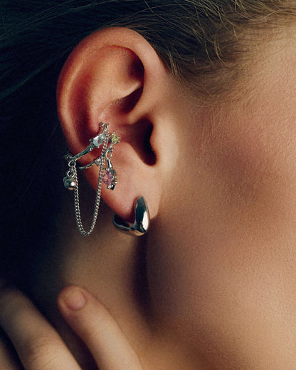 Gold and silver ear cuffs with dangling chains, charms, and colorful cubic zirconia stones. Non-pierced adjustable cartilage cuffs featuring teardrop and square-cut gems for a bold, playful, and trendy statement look.