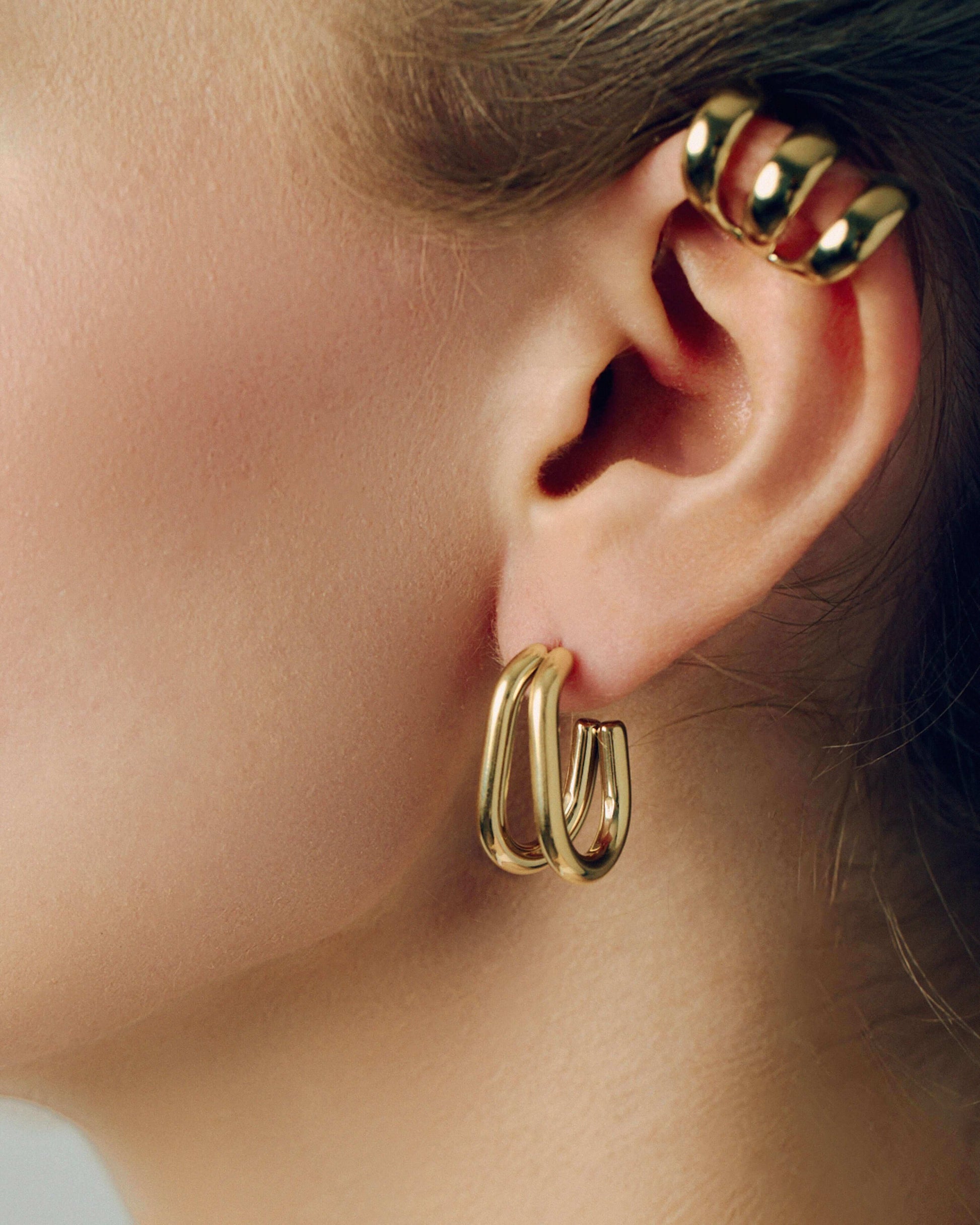 Gold double hoop earrings featuring two thick, sculptural curved bands with a polished high-shine finish. Modern layered design with secure post backs, creating a bold yet minimalist statement. Perfect for everyday wear or adding a stylish, contemporary touch to any outfit.