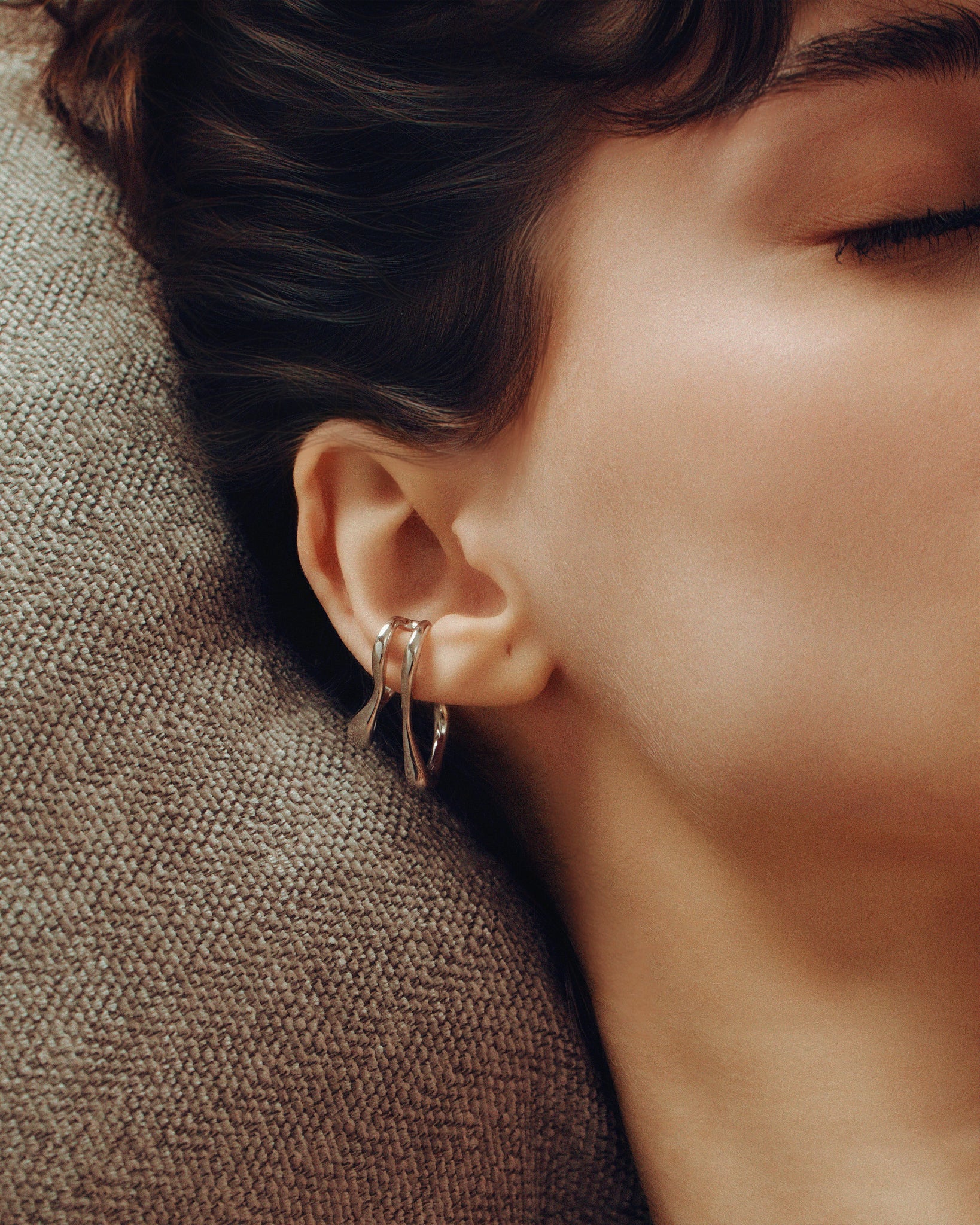 Model wearing oversized clip-on earrings in gold and silver versions. These sculptural, teardrop-shaped earrings feature a smooth, fluid form that wraps elegantly around the earlobe. Designed for non-pierced ears, they offer a bold, modern statement with a comfortable fit. Perfect for elevating everyday looks or adding a refined touch to evening outfits.