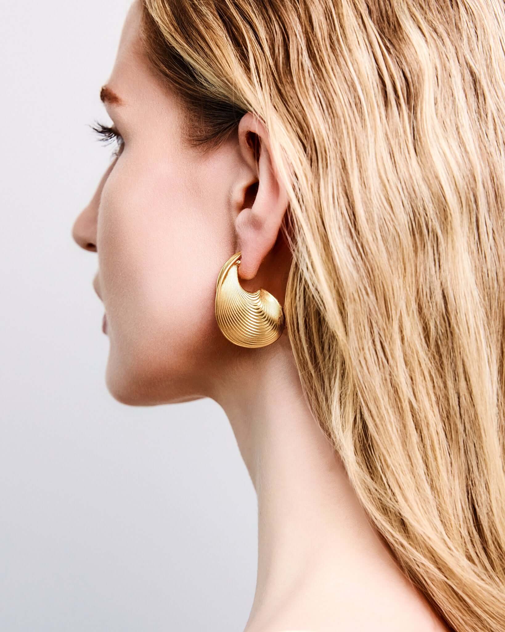 Sculptural ribbed hoop earrings in gold finish, bold textured statement hoops for women, modern curved hoop earrings, contemporary minimalist jewelry, chunky ribbed gold earrings for everyday wear or elevated evening styling