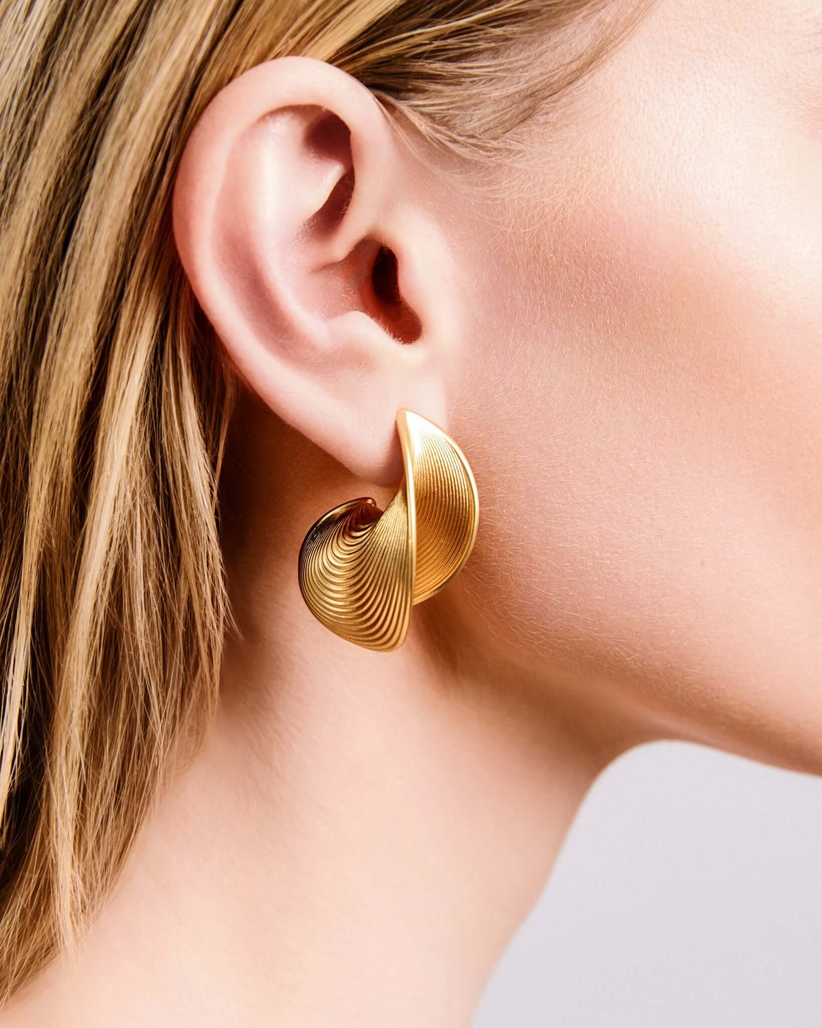 Sculptural ribbed hoop earrings in gold finish, bold textured statement hoops for women, modern curved hoop earrings, contemporary minimalist jewelry, chunky ribbed gold earrings for everyday wear or elevated evening styling