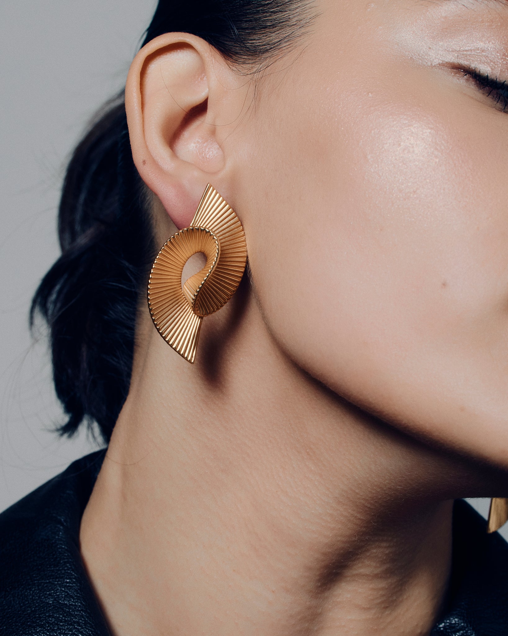 Pleated sculptural gold earrings featuring a twisted, folded design with fine ridged texture. These bold statement earrings have an open curved form that adds dimension and movement. Crafted in polished gold-tone metal, they bring a modern, architectural edge to any outfit — lightweight yet striking for everyday or occasion wear.
