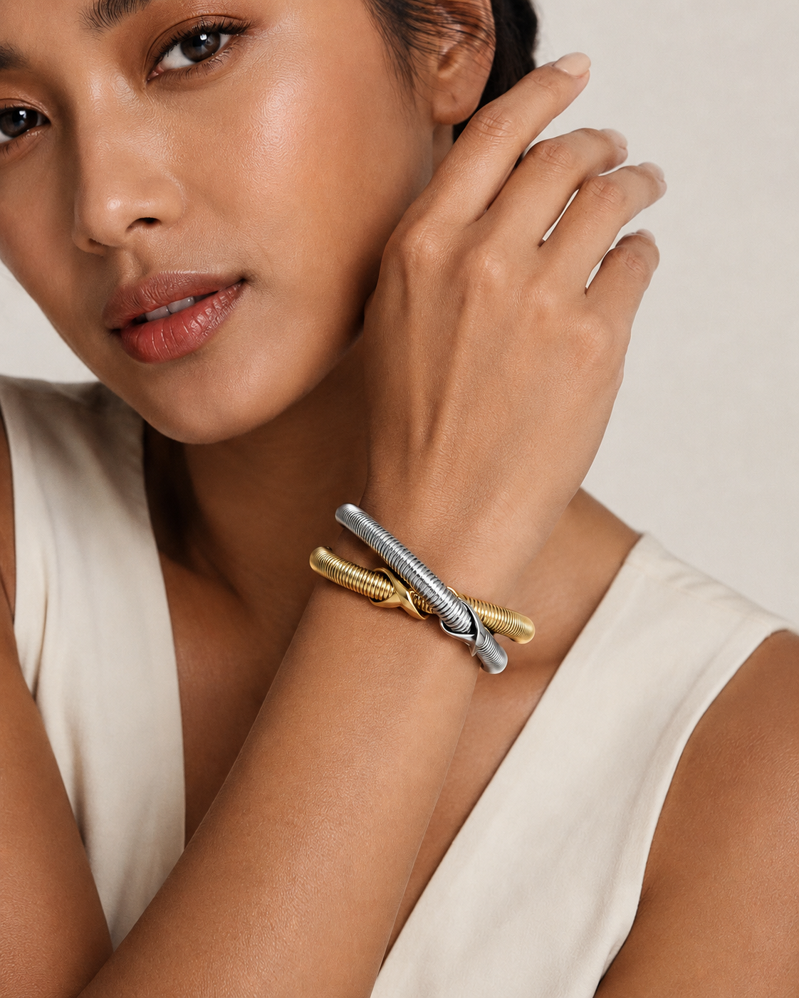 A close-up lifestyle shot of a model wearing a double-band bracelet with one gold-toned textured band and one silver-toned textured band crossing over a gold band.