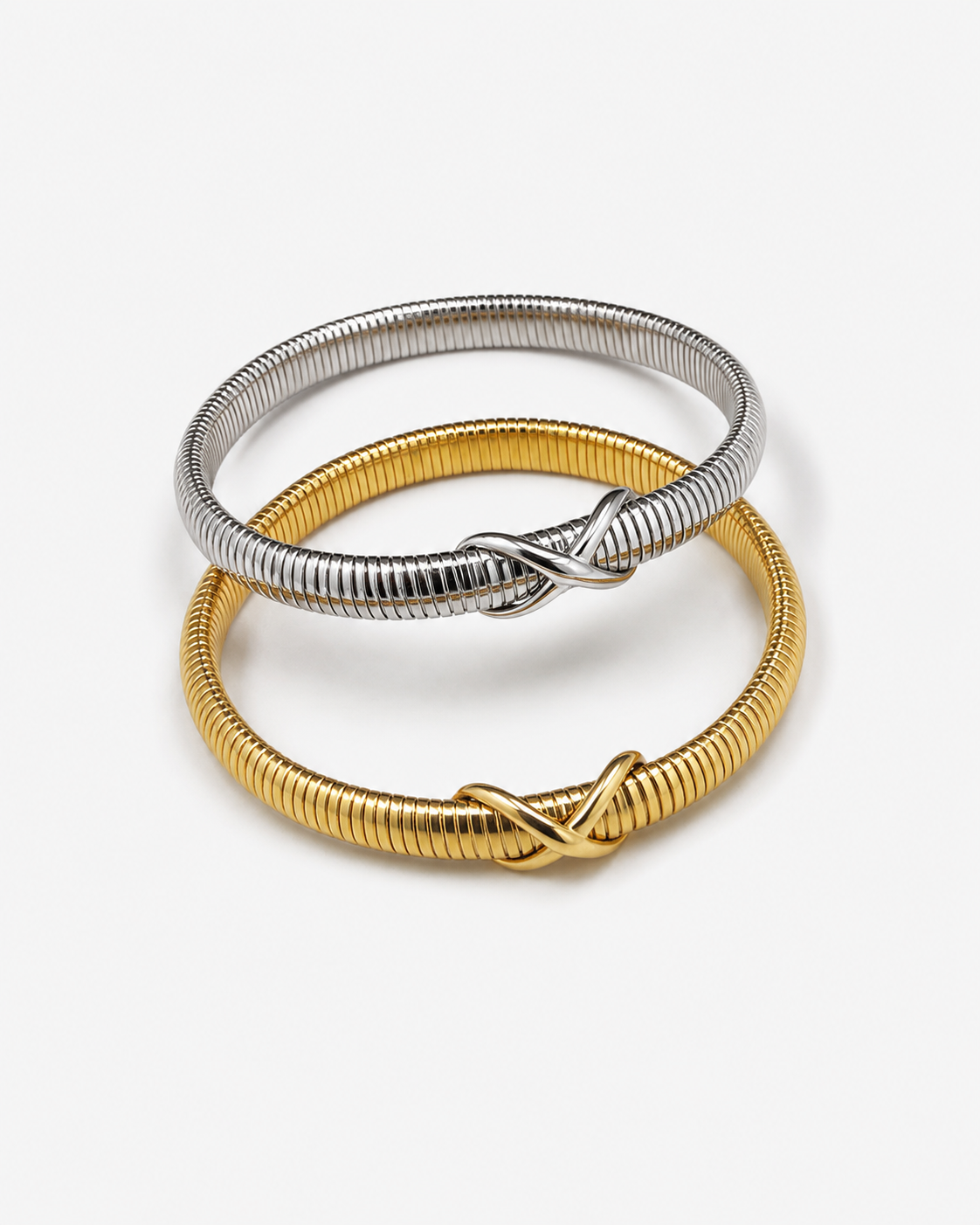 Two coiled bangle bracelets, one in silver and one in gold, each featuring an infinity knot design at the center, displayed on a clean white background.