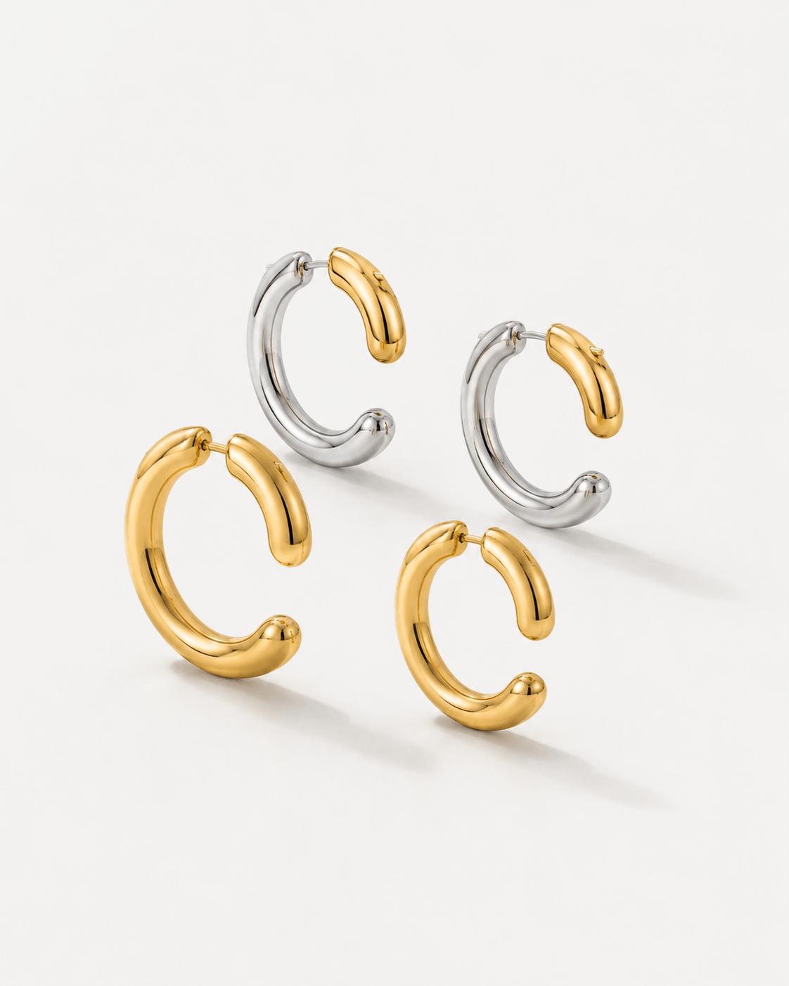 Two tone gold and silver 360 front back hoop earrings displayed on a soft neutral background. Modern sculptural shape hoop earrings with chunky curved silhouette, minimalist statement jewelry designed for contemporary everyday wear.