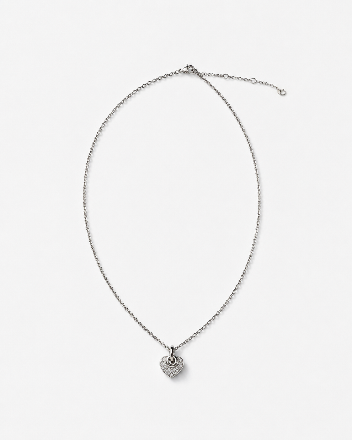 A silver-toned chain necklace with a small heart-shaped pendant paved with clear stones, displayed on a clean white background.