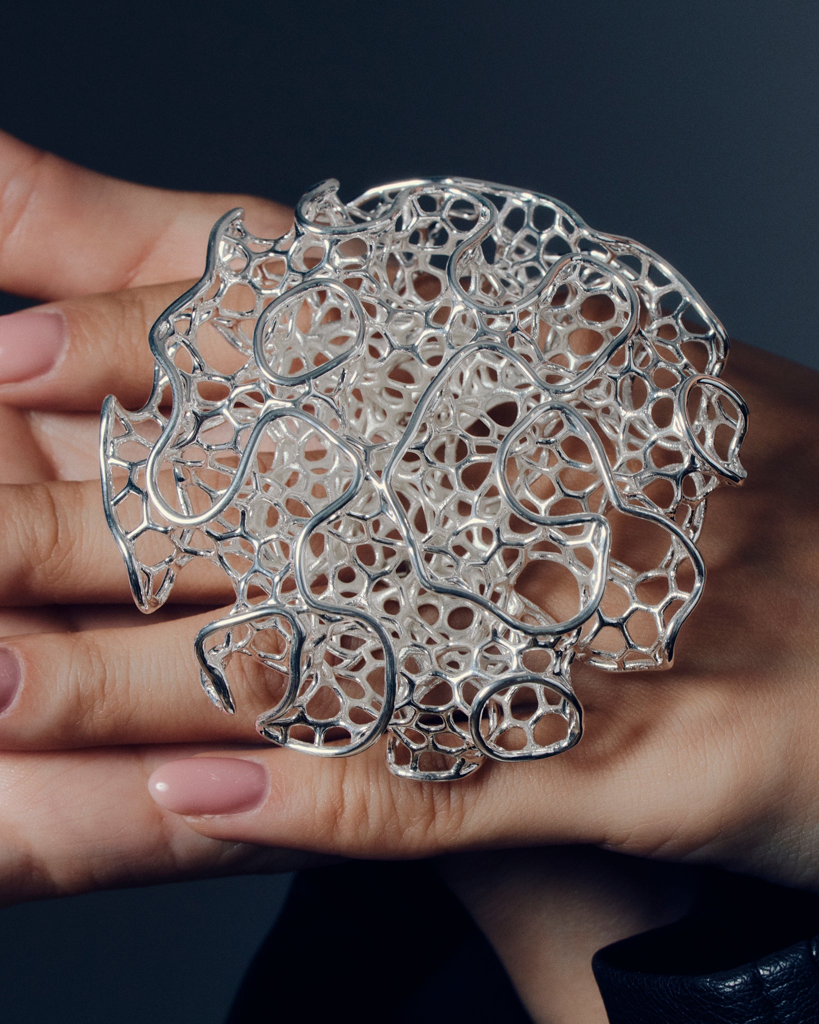 Close-up of a sculptural open-work statement ring featuring organic, lattice-like curves that flow across the fingers. The bold, artistic design catches light and shadow, creating a striking balance of size and airiness. Perfect for modern, contemporary, and architectural jewelry lovers who appreciate wearable art.