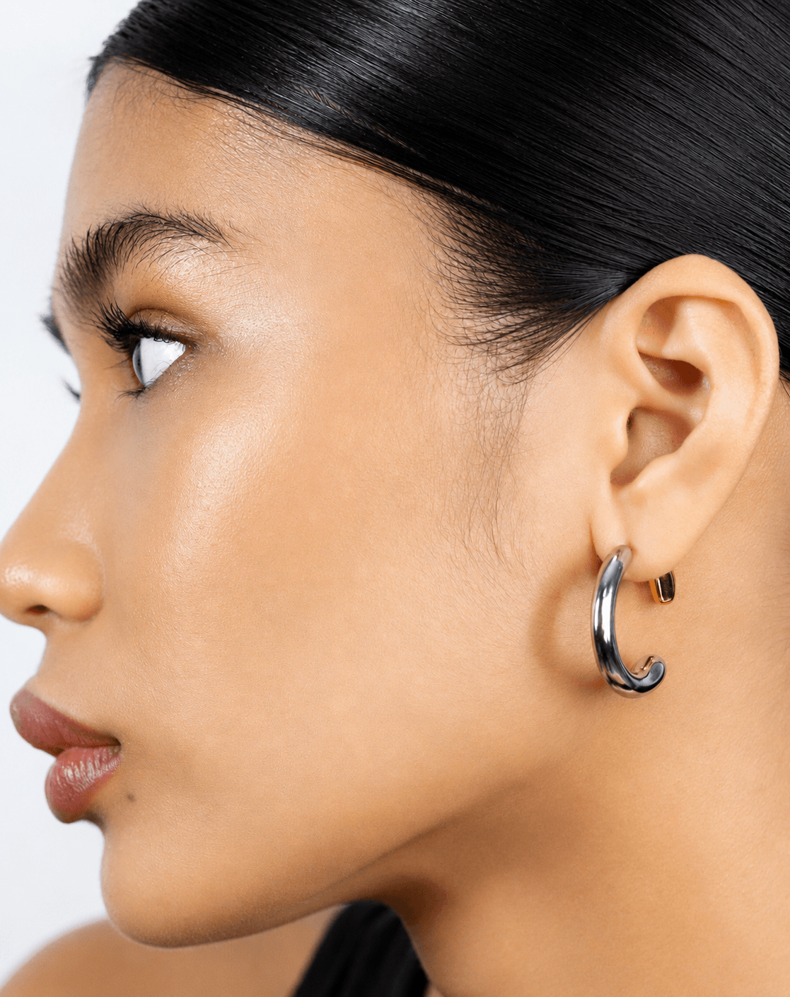 Two tone gold and silver 360 front back hoop earrings displayed on a soft neutral background. Modern sculptural shape hoop earrings with chunky curved silhouette, minimalist statement jewelry designed for contemporary everyday wear.