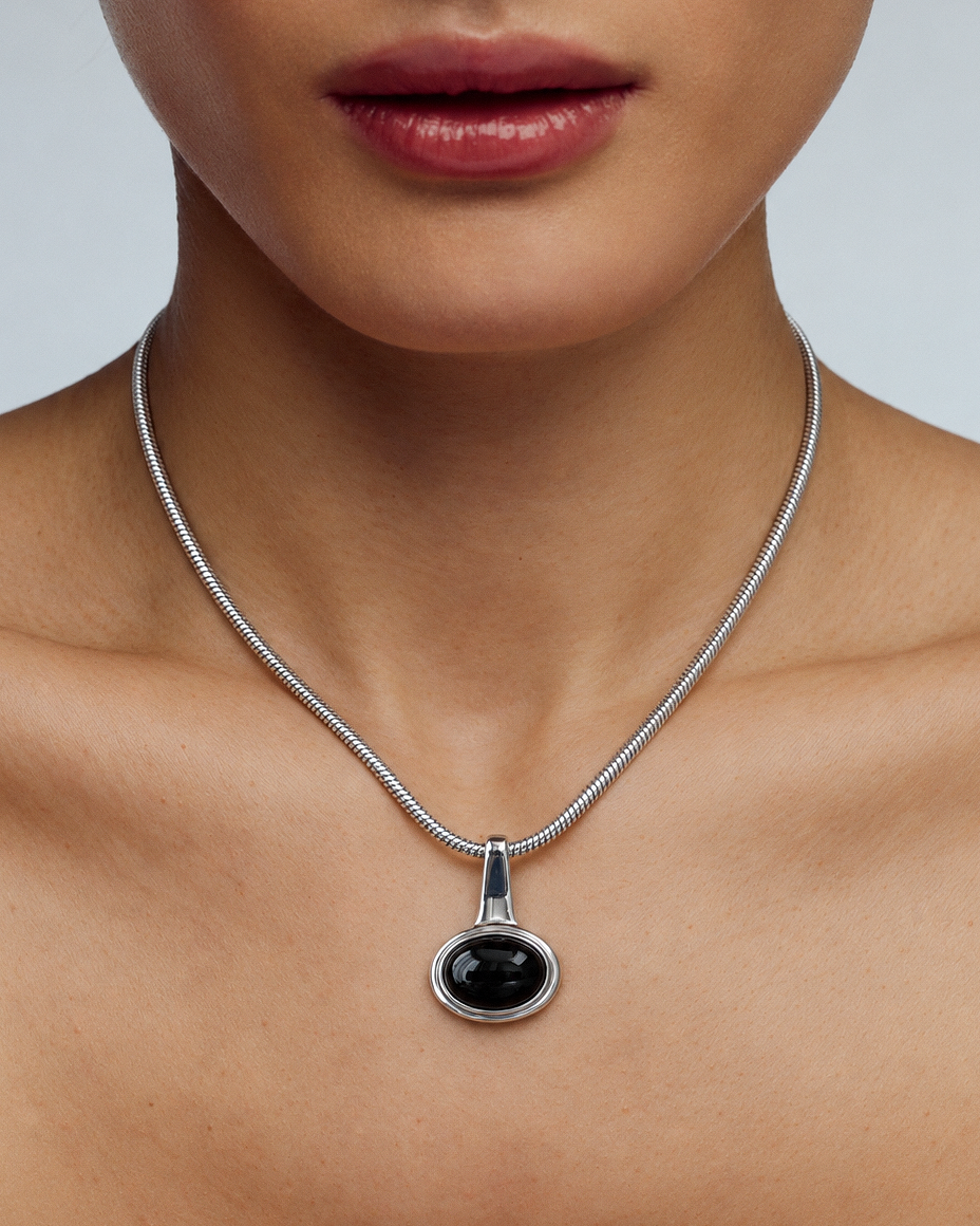 A close-up of a model wearing a silver snake chain necklace with a round black onyx pendant.