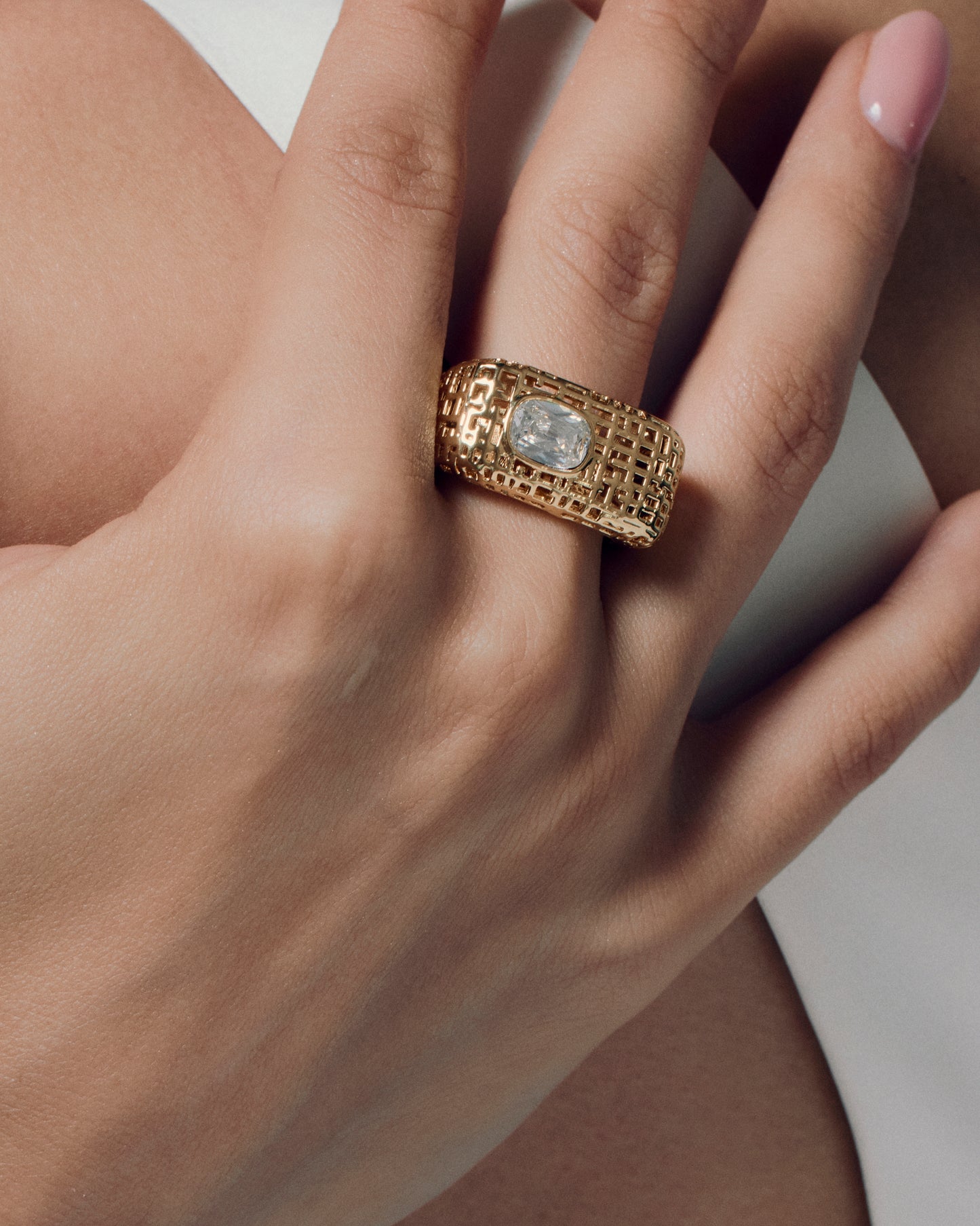 Model wearing open work square gold ring with clear stone, showing the chunky sculptural texture and modern grid-pattern design. A bold gold statement ring that elevates everyday style or evening wear, highlighting its geometric shape and luxurious finish for a refined yet artistic look.