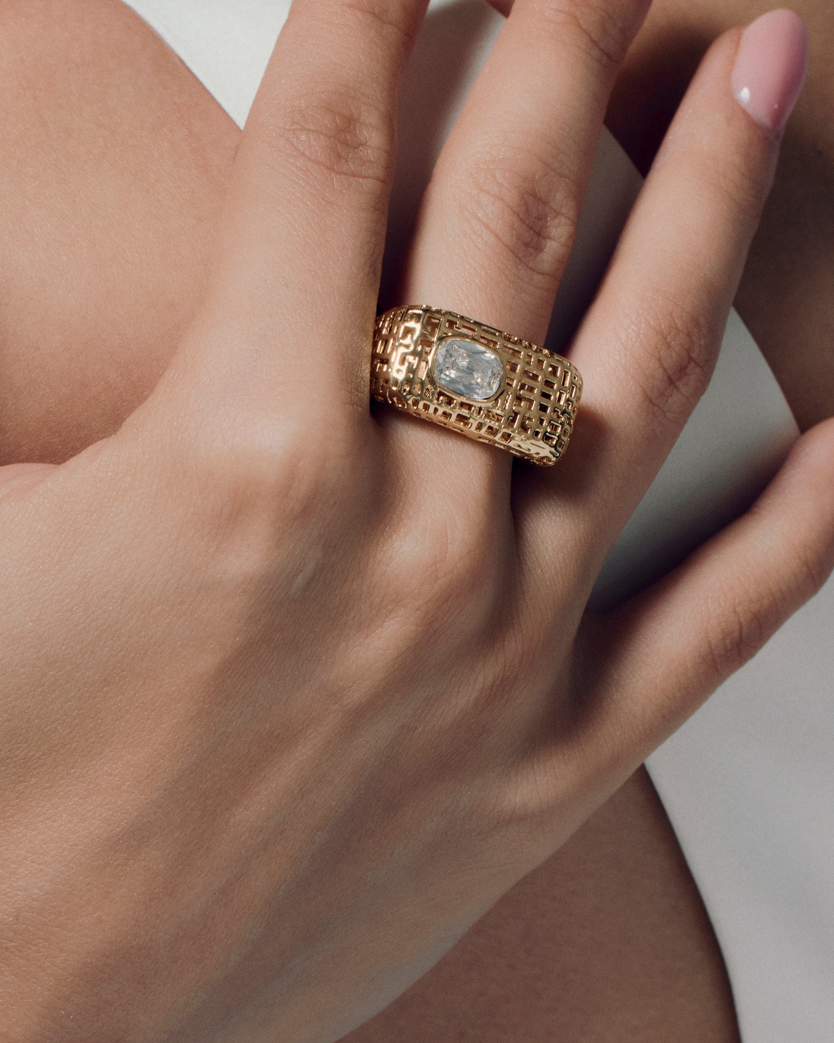 Model wearing open work square gold ring with clear stone, showing the chunky sculptural texture and modern grid-pattern design. A bold gold statement ring that elevates everyday style or evening wear, highlighting its geometric shape and luxurious finish for a refined yet artistic look.