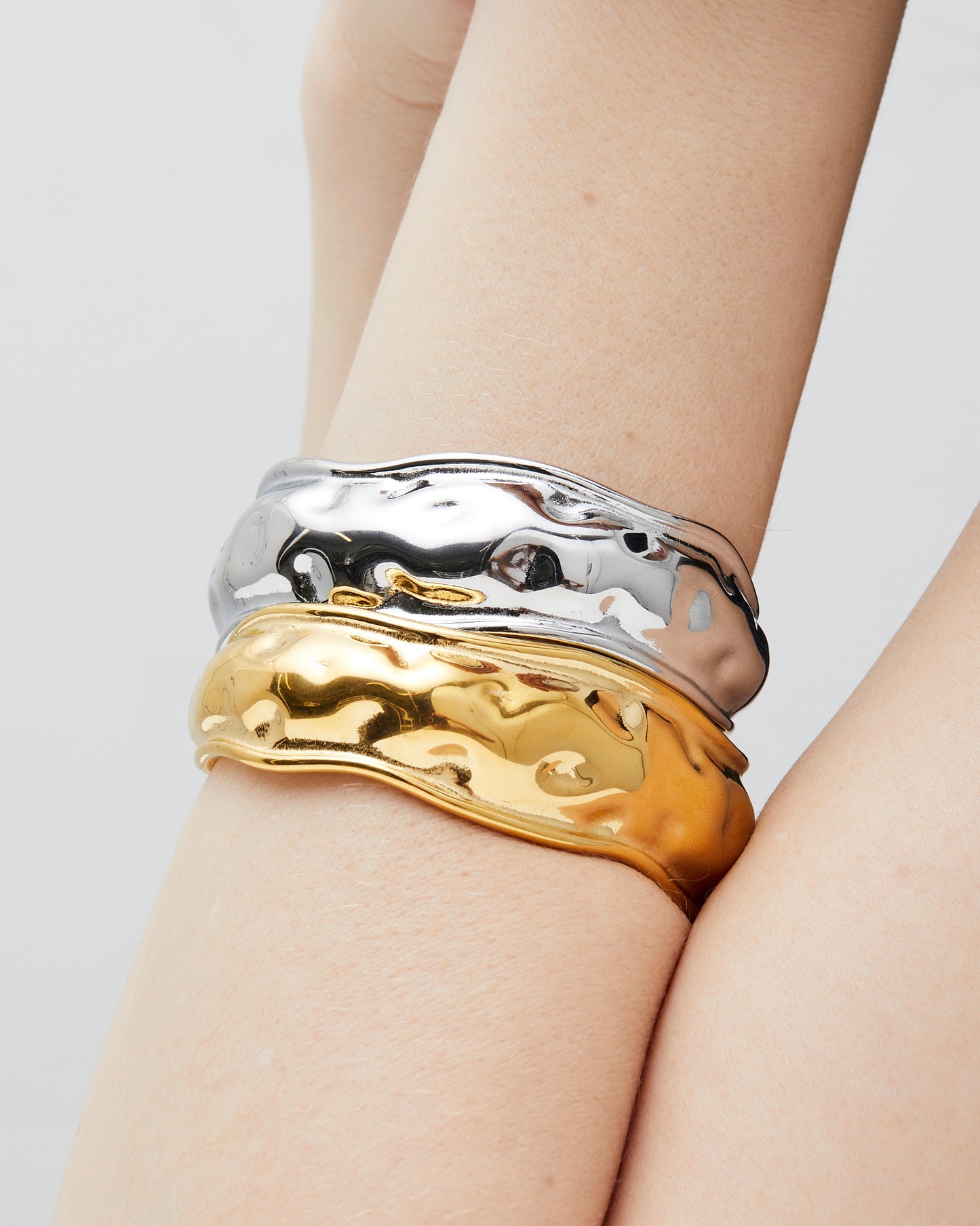 Gold or silver wavy cuff bracelets stacked on wrist, featuring a sculptural organic design with high-polish mirror finish and hammered texture — modern statement bangles crafted from durable Italian metal.