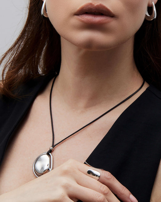 Oversized bean pendant on a polished black tie chain with 18k gold or silver finish, adjustable length, sleek modern minimalist design.