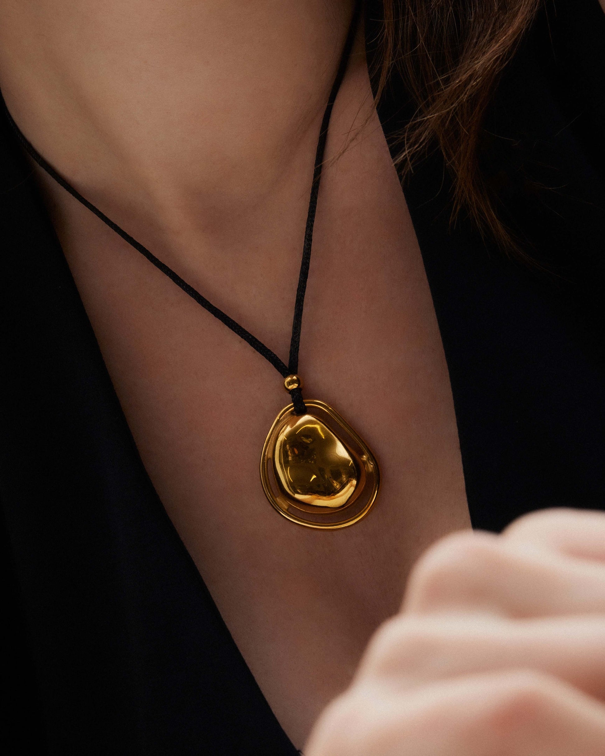 Oversized bean pendant on a polished black tie chain with 18k gold or silver finish, adjustable length, sleek modern minimalist design.