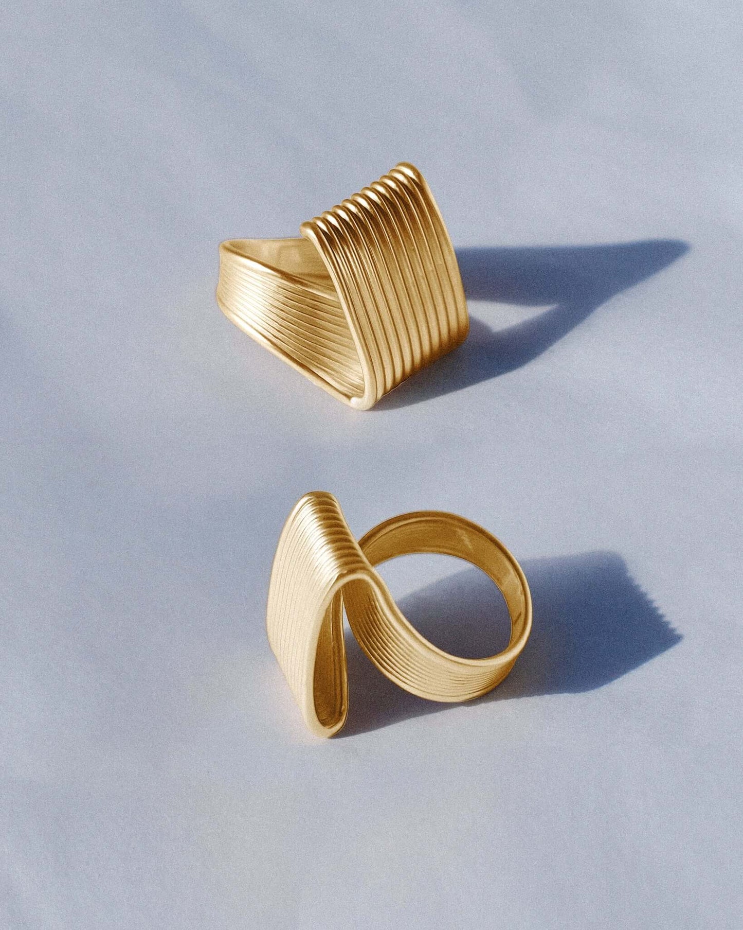 Pleated square gold ring featuring fine ridged detailing that flows seamlessly across the face and band. This sculptural textured ring combines a bold square shape with a soft pleated design, balancing modern geometry and fluid form. Crafted in polished gold-tone metal, it’s a statement piece for everyday or occasion wear.