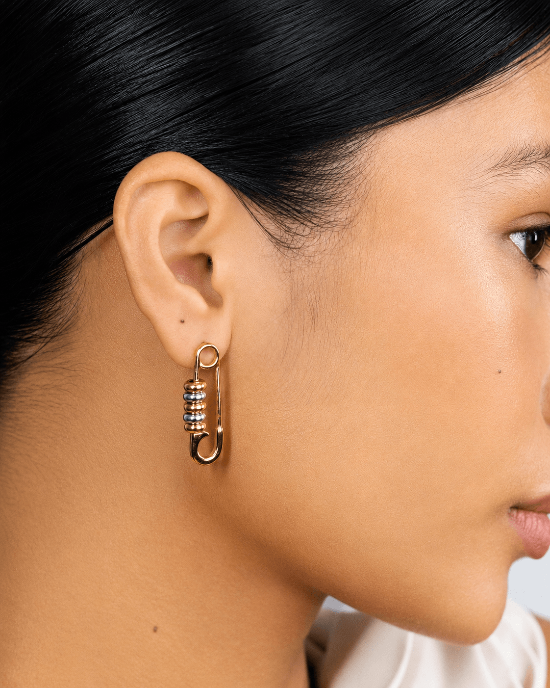 Gold safety pin earrings with silver bead details worn on ear, chunky statement earrings for women, modern two tone jewelry, edgy minimalist gold hoop earrings, trendy everyday fashion accessory, unique punk inspired earrings, stainless steel safety pin d