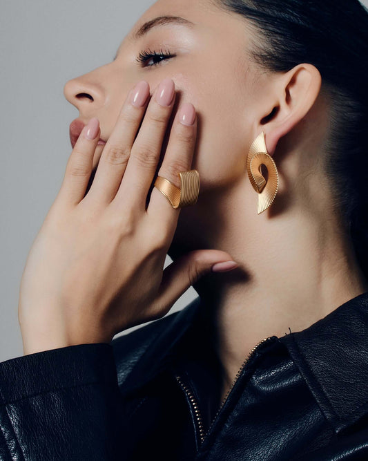 Pleated square gold ring featuring fine ridged detailing that flows seamlessly across the face and band. This sculptural textured ring combines a bold square shape with a soft pleated design, balancing modern geometry and fluid form. Crafted in polished gold-tone metal, it’s a statement piece for everyday or occasion wear.