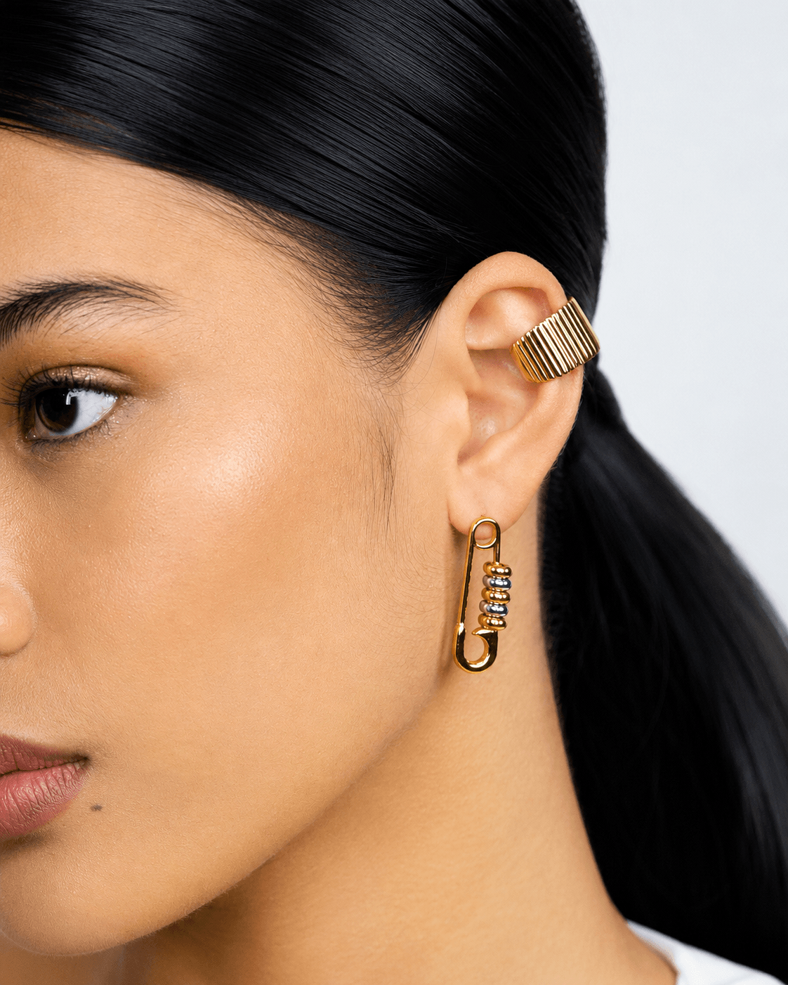 Gold safety pin earrings with silver bead details worn on ear, chunky statement earrings for women, modern two tone jewelry, edgy minimalist gold hoop earrings, trendy everyday fashion accessory, unique punk inspired earrings, stainless steel safety pin d
