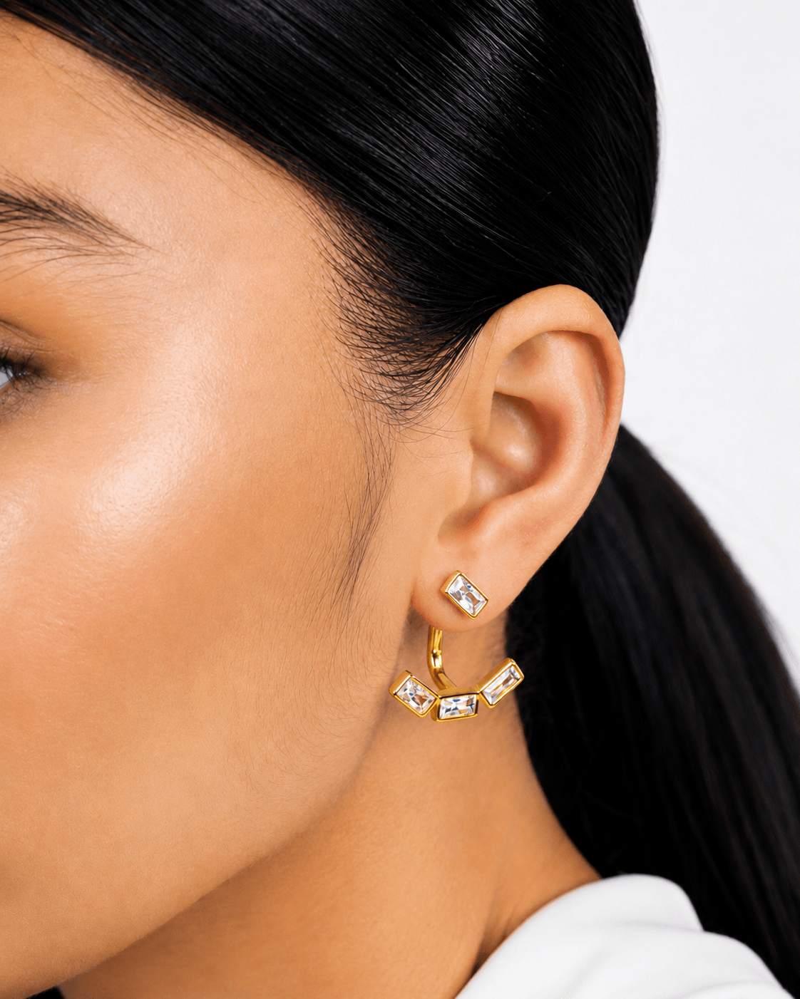 Detachable baguette zircon ear jacket earrings in gold finish displayed on a soft neutral background. Modern geometric stud earrings with removable ear jacket design, featuring sparkling rectangular CZ stones and minimalist contemporary styling for everyday wear and statement looks.