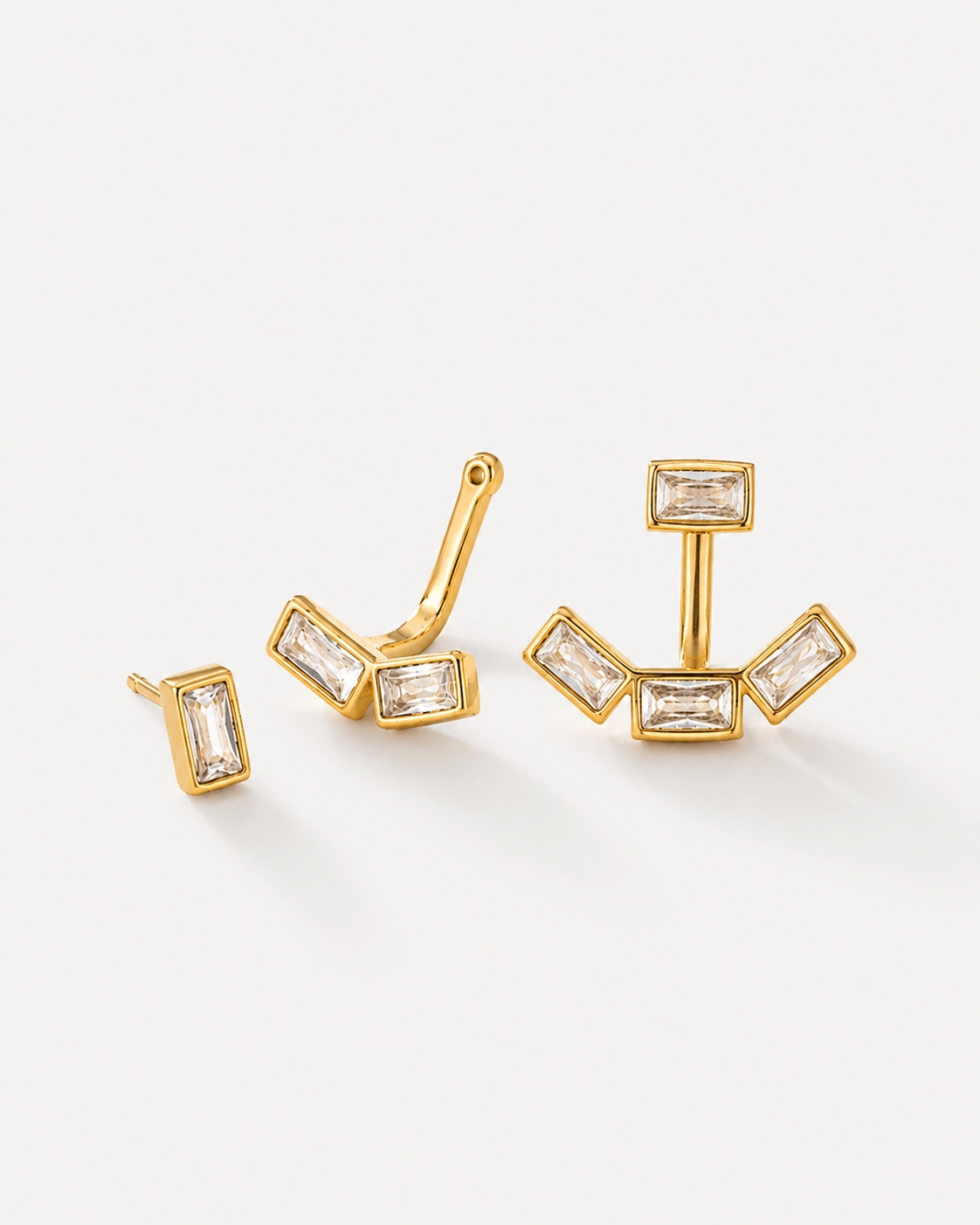 Detachable baguette zircon ear jacket earrings in gold finish displayed on a soft neutral background. Modern geometric stud earrings with removable ear jacket design, featuring sparkling rectangular CZ stones and minimalist contemporary styling for everyday wear and statement looks.